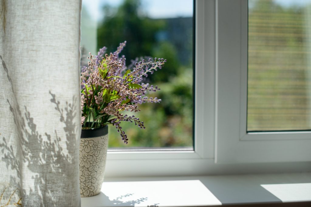 Image of window with a flower in a pot and curtain in the room.