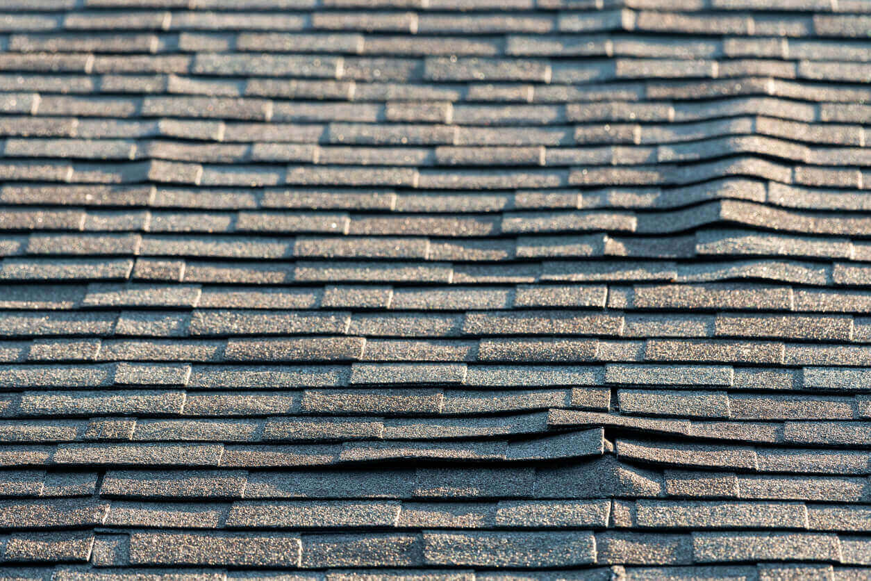 A view of a residential roof with architectural asphalt shingles that with various issues that can be signs of water damage and poor workmanship. The buckling of the shingles could be signs of the sheathing can be warping or delaminating from water penetration, which leads to a reroof.