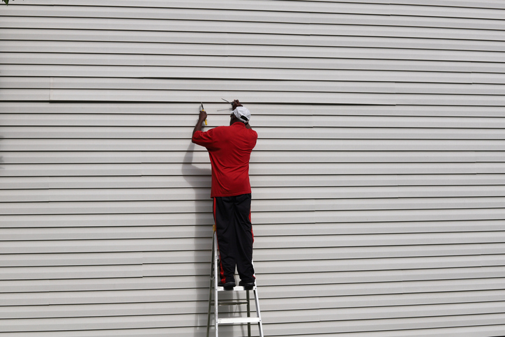 man on a ladder and fixing vinyl siding on a house