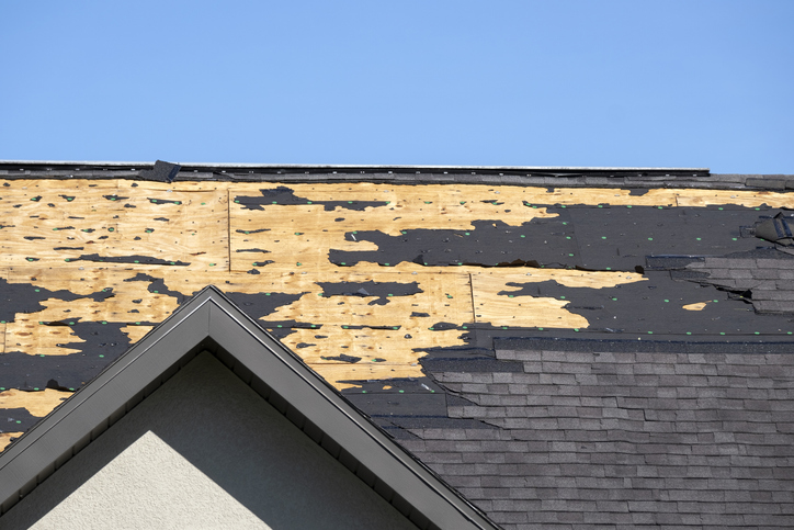 Damaged house roof with missing shingles after hurricane. Consequences of natural disaster.