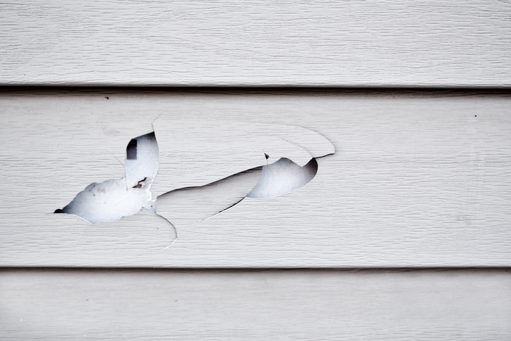 Close up of a cracked and broken beige vinyl siding of a house