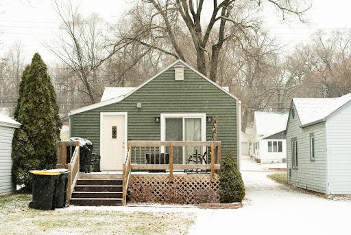 Exterior back side of a tiny house with a wooden deck during a snow fall