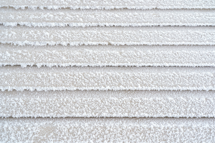 The wall of the building is covered with beige plastic clapboard. There is white fluffy frost on the surface of the siding. Background. Texture.