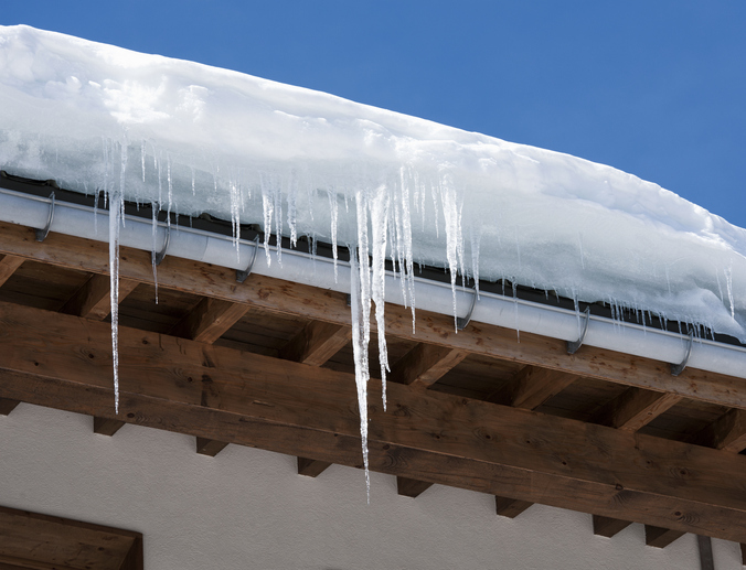 Long icicles and snow overhaning the roof and gutter of a building.