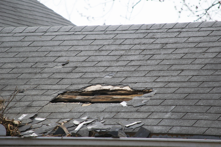 Roof of a residential house showing damage, multiple layers of shingles, missing shingles