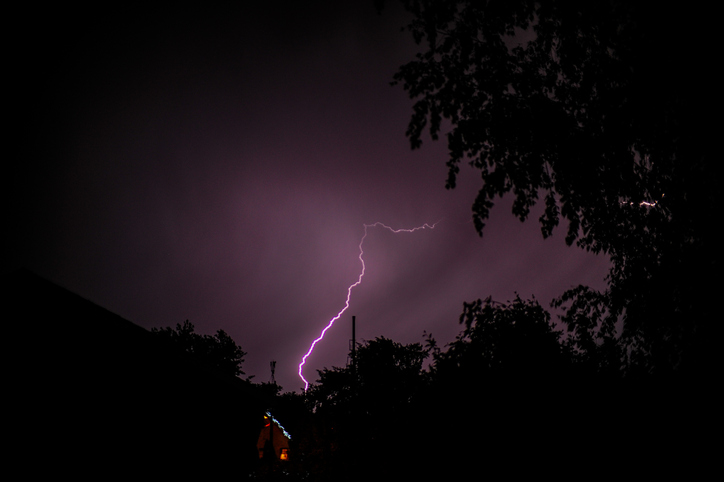 A lightning strike at night with trees in the foreground