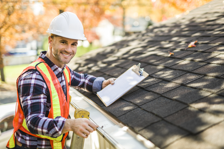 A man with hard hat standing on steps inspecting house roof