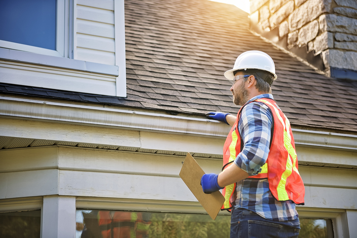 A man with hard hat standing on steps inspecting house roof
